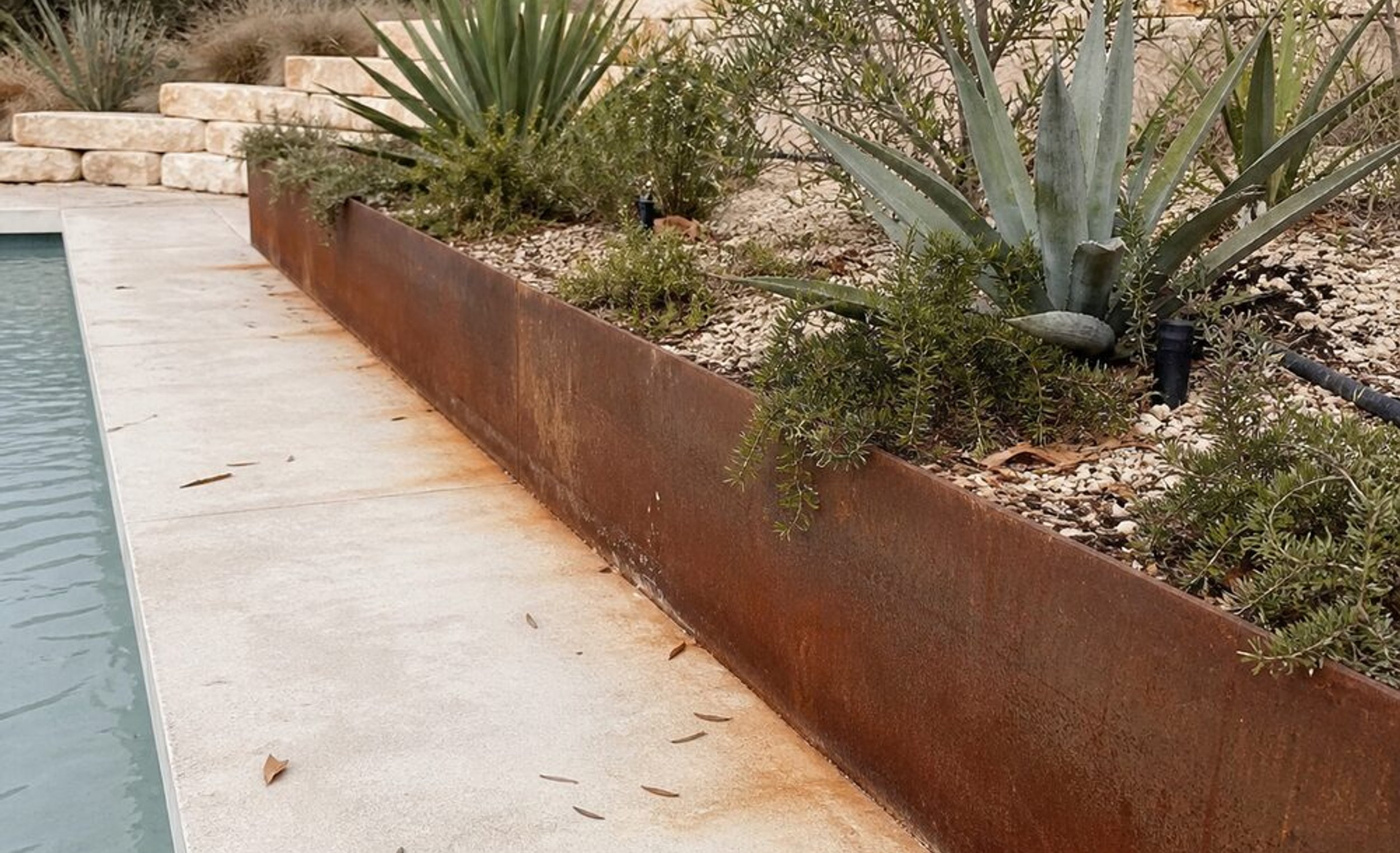 Light-colored concrete pool deck running between a pool and a steel planter